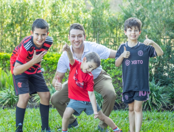 Doctor Weiss smiling and giving thumbs up outdoors with three kids wearing soccer uniforms